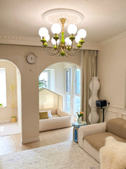 Modern living room with gold and green 8-light chandelier, beige sofa, and cozy sunlit nook with house-shaped bed