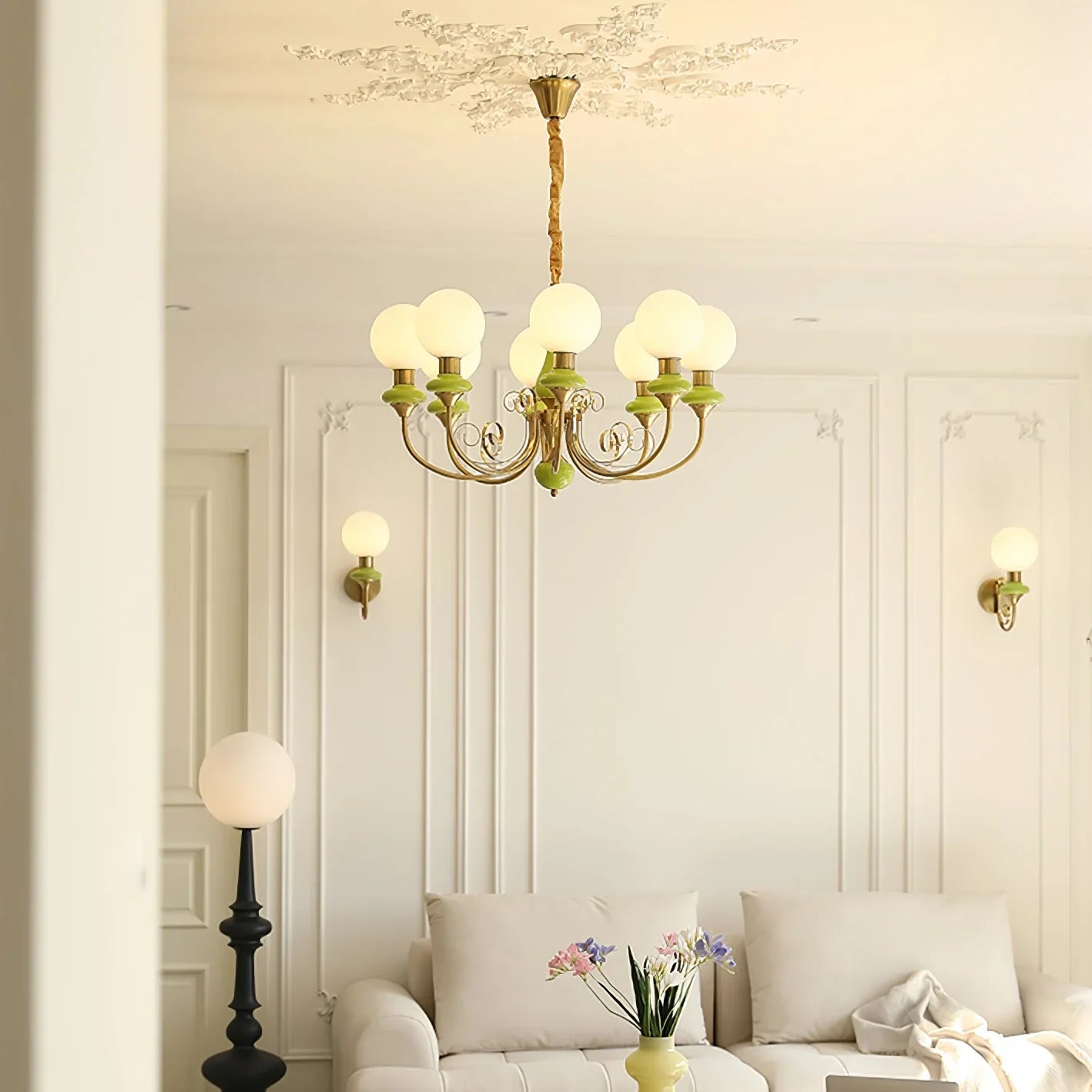 Elegant living room with gold and green multi-globe chandelier, beige sofa, wall sconces, and decorative molding