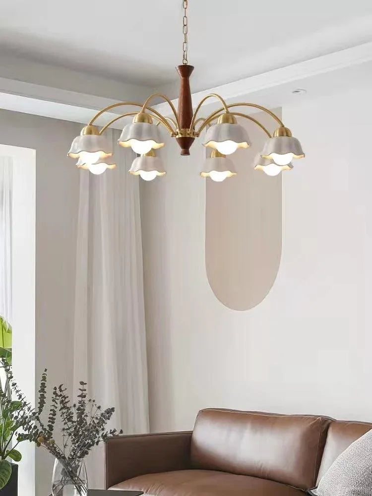 Modern brass chandelier with six white petal-shaped shades and wooden center hanging above brown leather sofa in minimalist living room