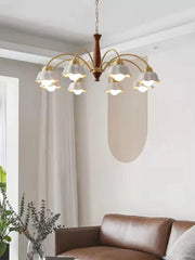 Modern brass chandelier with six white petal-shaped shades and wooden center hanging above brown leather sofa in minimalist living room