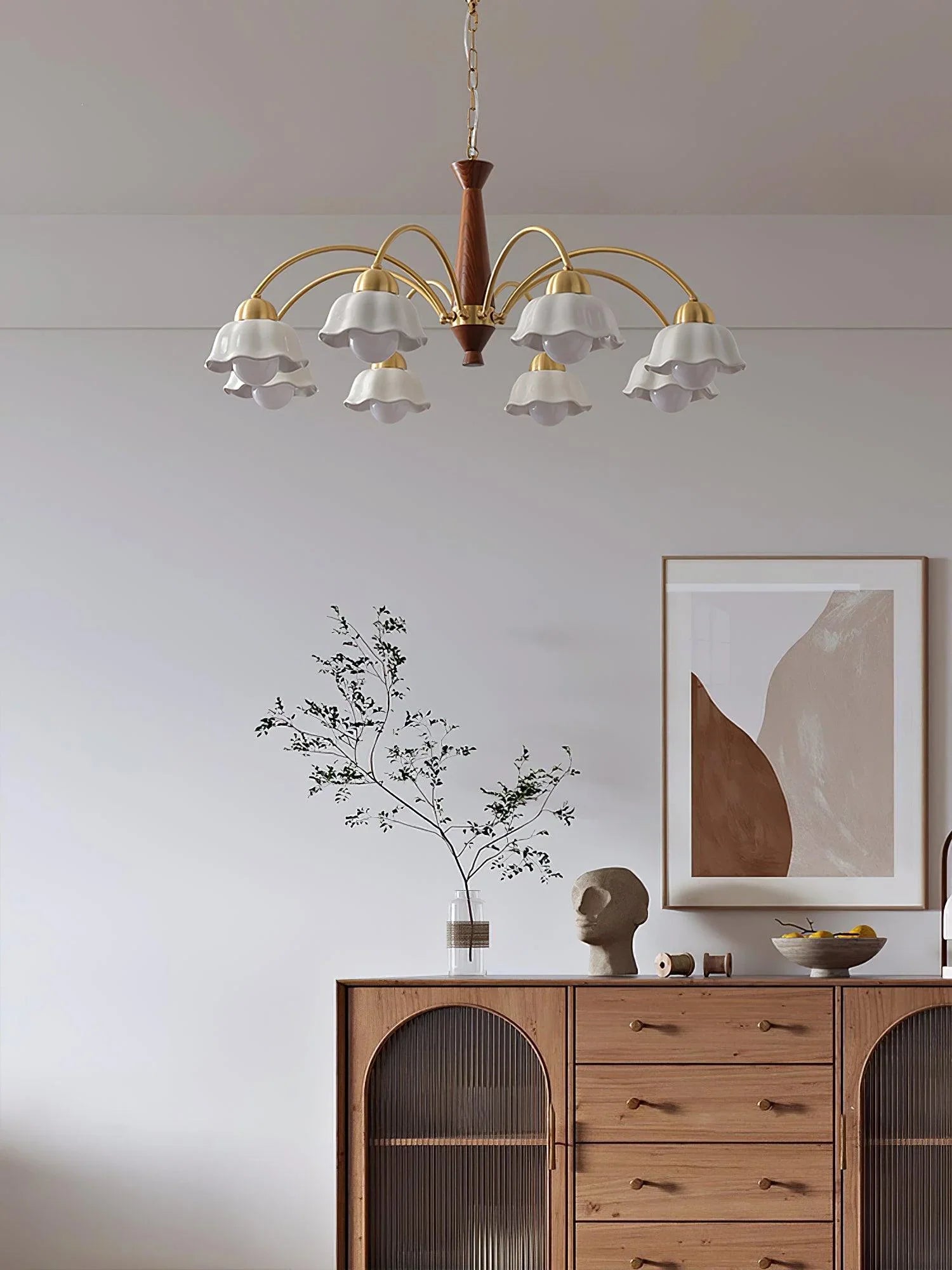Swedish modern brass chandelier with white flower-shaped glass shades hanging above wooden cabinet in minimalist room
