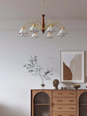 Swedish modern brass chandelier with white flower-shaped glass shades hanging above wooden cabinet in minimalist room