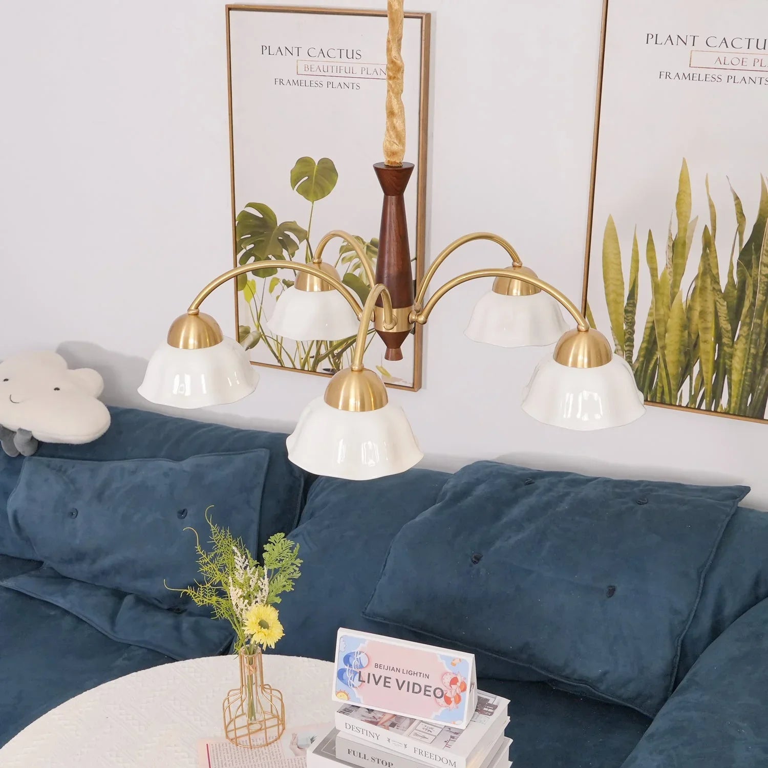 Modern 5-head brass chandelier with white glass lampshades over blue sofa and plant wall art