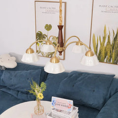 Modern 5-head brass chandelier with white glass lampshades over blue sofa and plant wall art