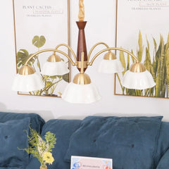 Modern 3-head brass and walnut wood chandelier with white floral glass shades over blue sofa and botanical wall art