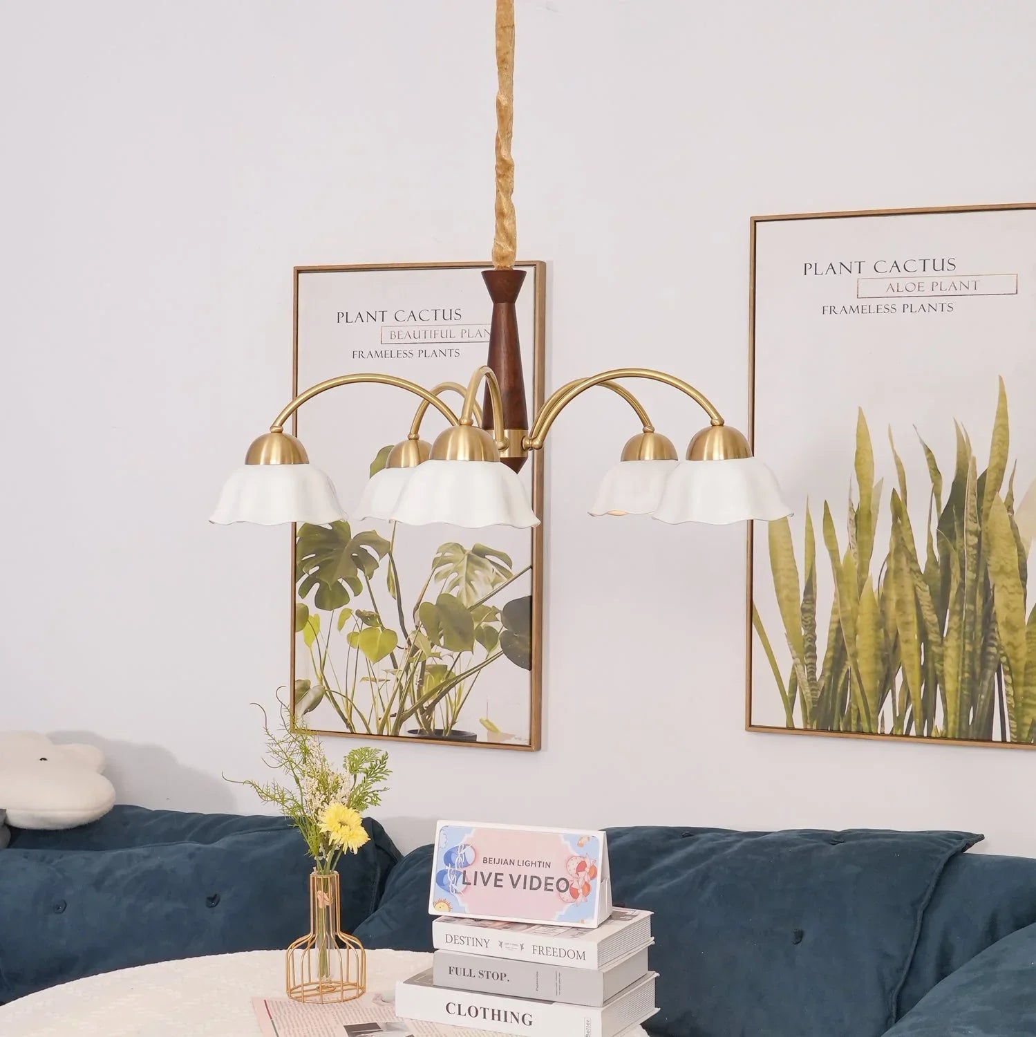 Swedish modern 3-head chandelier with brass and walnut wood and white flower-shaped shades over a cozy blue velvet sofa and decorative plant posters