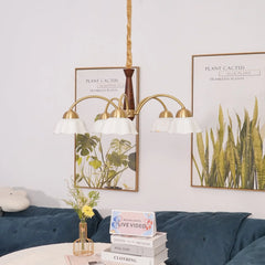 Swedish modern 3-head chandelier with brass and walnut wood and white flower-shaped shades over a cozy blue velvet sofa and decorative plant posters