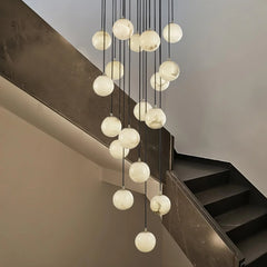 Modern cluster chandelier with 19 alabaster globe lights hanging in a staircase with dark steps