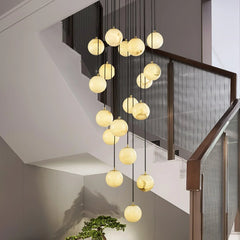 Modern cluster chandelier with alabaster ball pendants hanging in a staircase with gray walls and glass railing