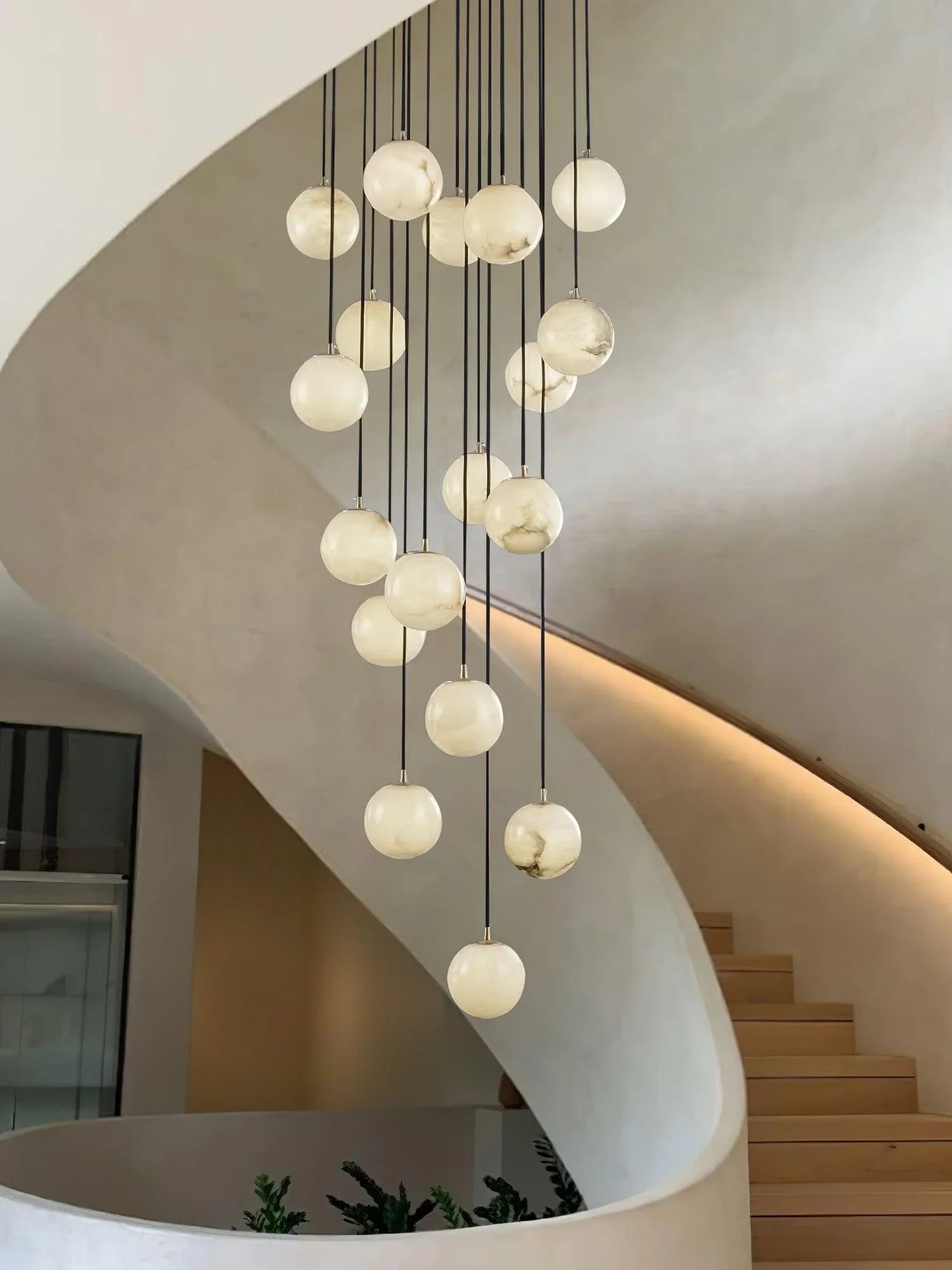 Modern cluster chandelier with alabaster ball pendants hanging in a minimal curved staircase interior