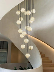 Modern cluster chandelier with alabaster ball pendants hanging in a minimal curved staircase interior