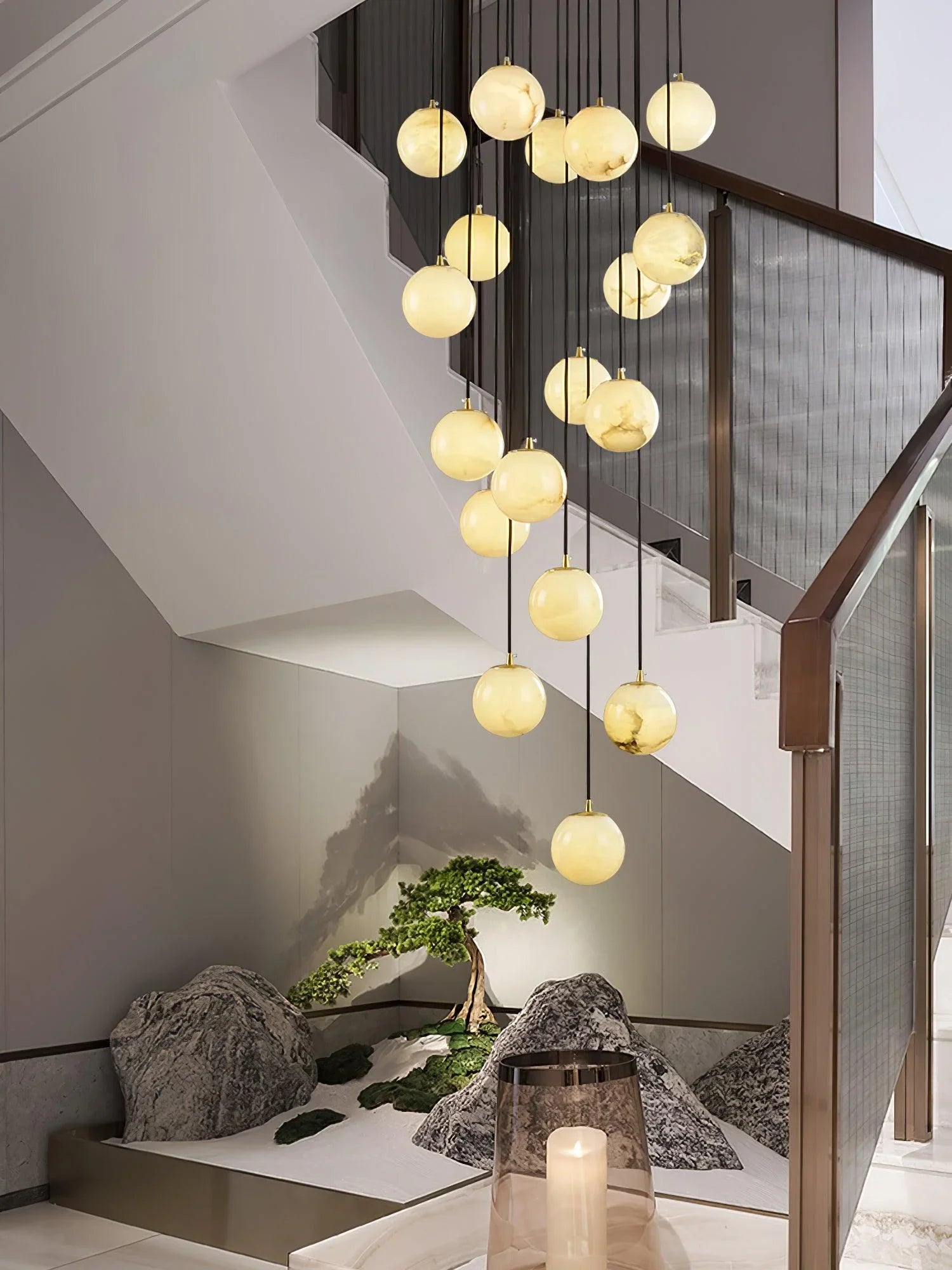 Modern pendant lamp chandelier with multiple alabaster ball lights hanging in elegant stairwell over decorative stones and small bonsai tree