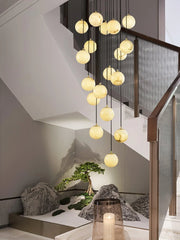 Modern pendant lamp chandelier with multiple alabaster ball lights hanging in elegant stairwell over decorative stones and small bonsai tree