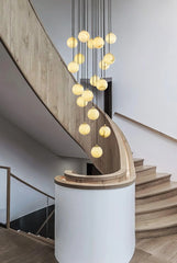 Modern chandelier with multiple alabaster ball pendants hanging above curved wooden staircase in minimalist interior