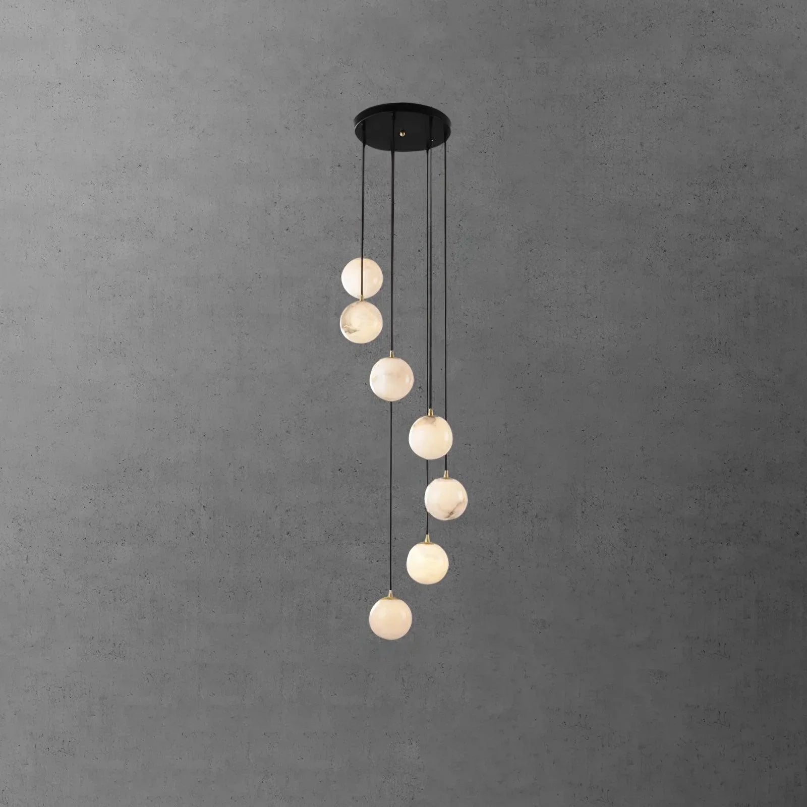 Modern black pendant chandelier with seven alabaster glass globes hanging at varying lengths against gray wall