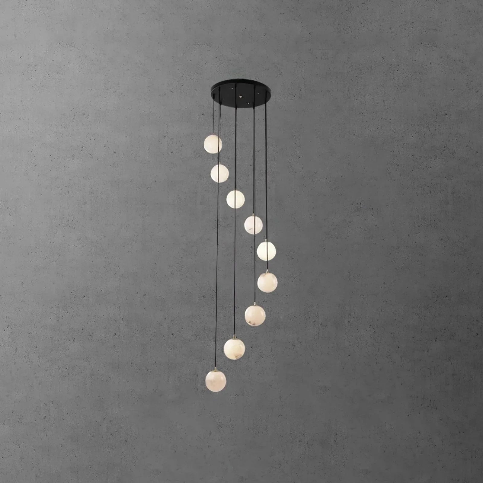 Modern pendant chandelier with nine alabaster ball lights hanging from a round black canopy on gray concrete wall