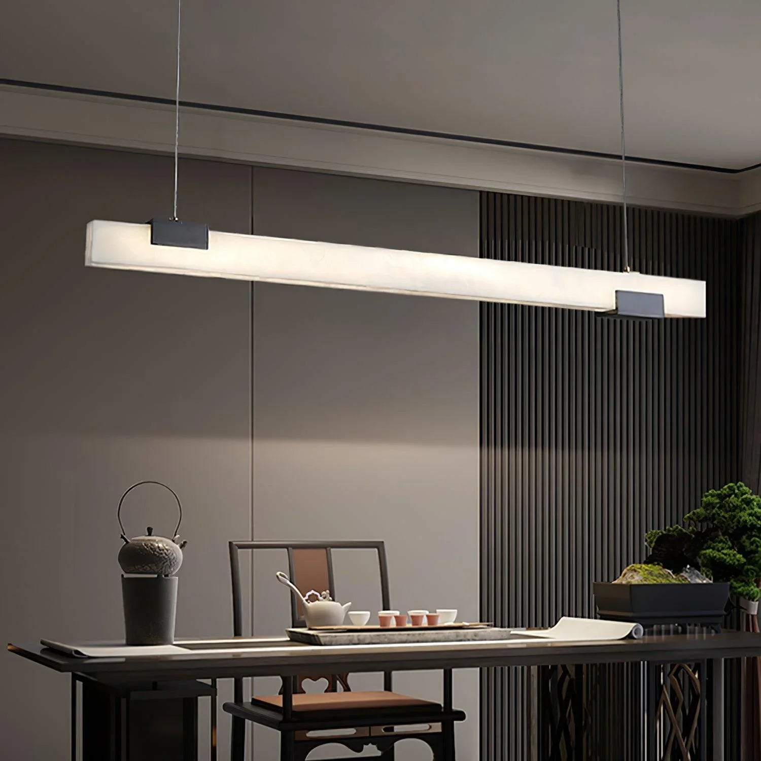 Modern minimalist black and white elongated pendant lamp over dining table with teapot set and greenery