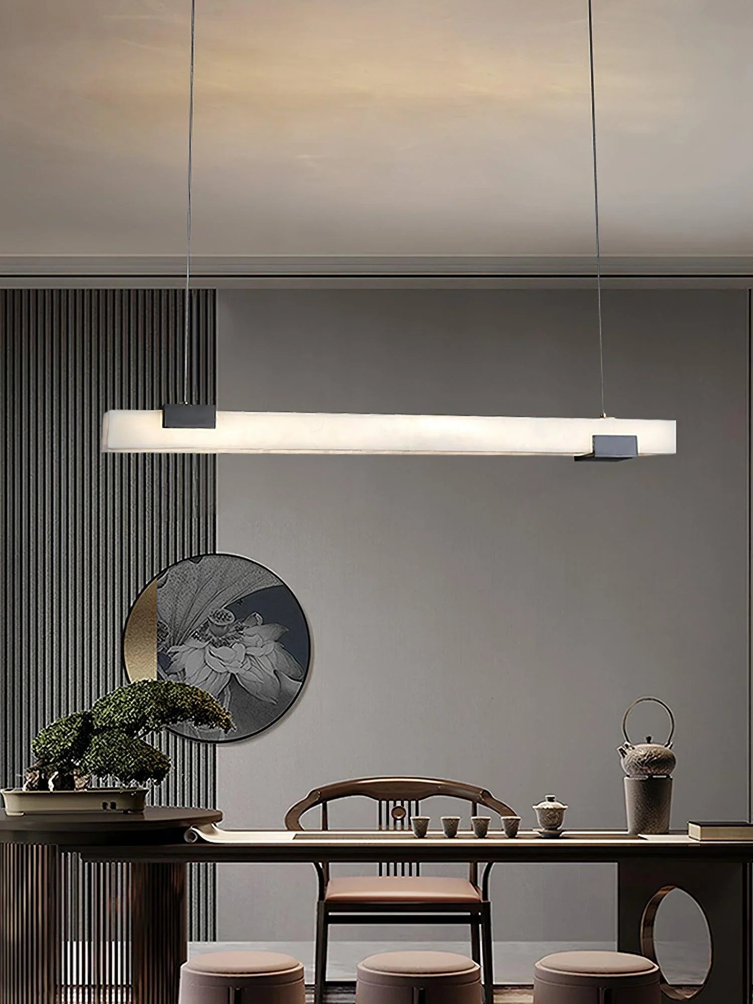 Modern rectangular alabaster pendant lamp hanging above minimalist dining table with bonsai and tea set
