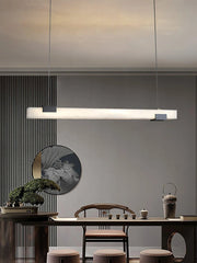 Modern rectangular alabaster pendant lamp hanging above minimalist dining table with bonsai and tea set