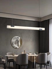 Modern rectangular alabaster pendant chandelier with warm light over marble dining table in minimalist dining room