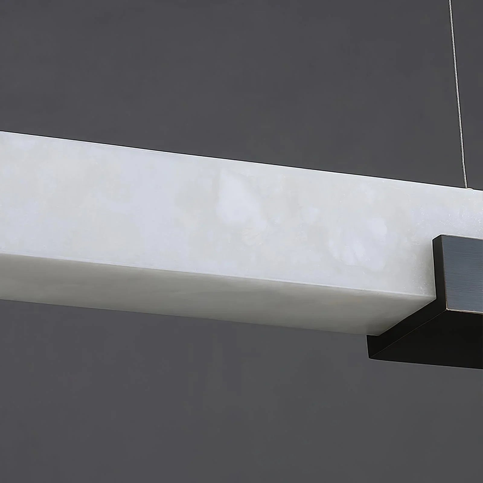 Modern rectangular alabaster pendant light with black metal accents hanging against gray background