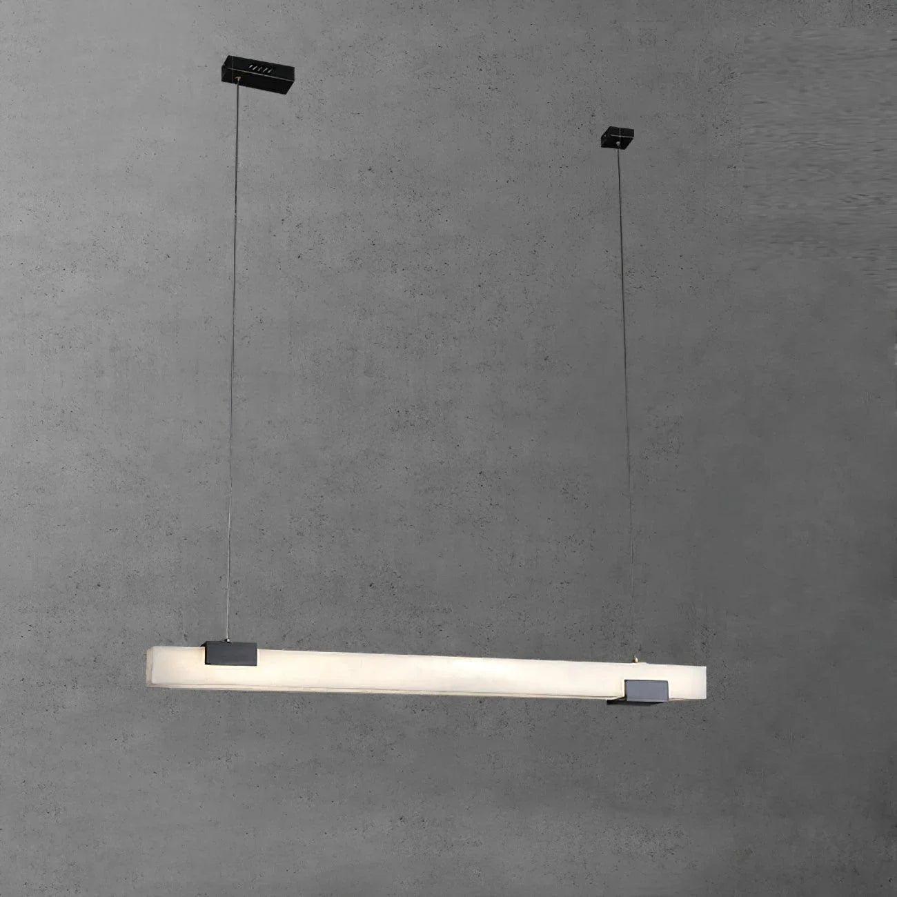 Modern linear pendant lamp with alabaster shade and black metal accents hanging against gray wall