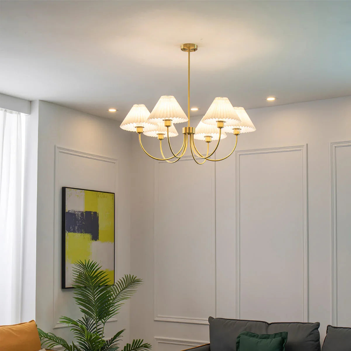 Modern brass chandelier with four white pleated shades hanging in a stylish living room