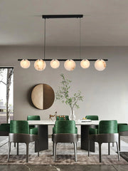 Modern dining room with green velvet chairs, marble table, brass chandelier with six round alabaster lampshades