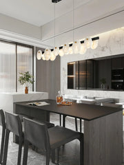 Modern dining room with black table, dark chairs, marble accents, and a long pendant chandelier with white glass discs