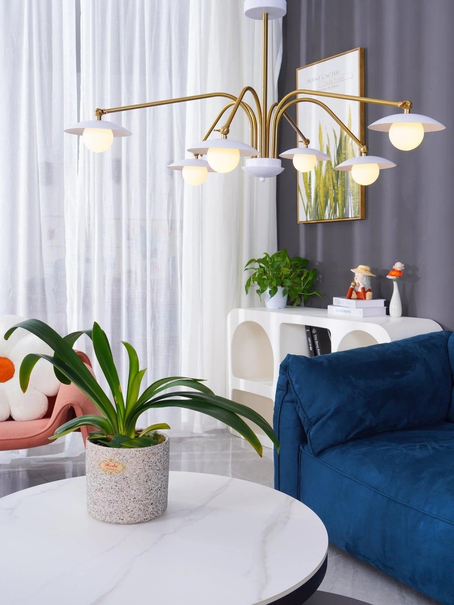 Modern chandelier with six white globe lights and gold arms in stylish living room with blue sofa, plants, and white curtains