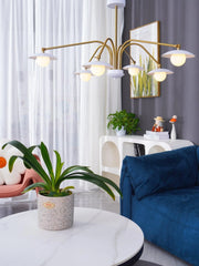 Modern chandelier with six white globe lights and gold arms in stylish living room with blue sofa, plants, and white curtains