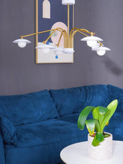 Modern 6-head gold and white chandelier hanging above blue velvet sofa in stylish living room with abstract wall art and green plant
