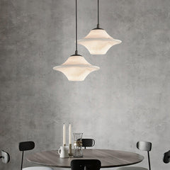 Modern black and white saucer alabaster pendant lamps hanging above a round wooden dining table with black chairs and candles