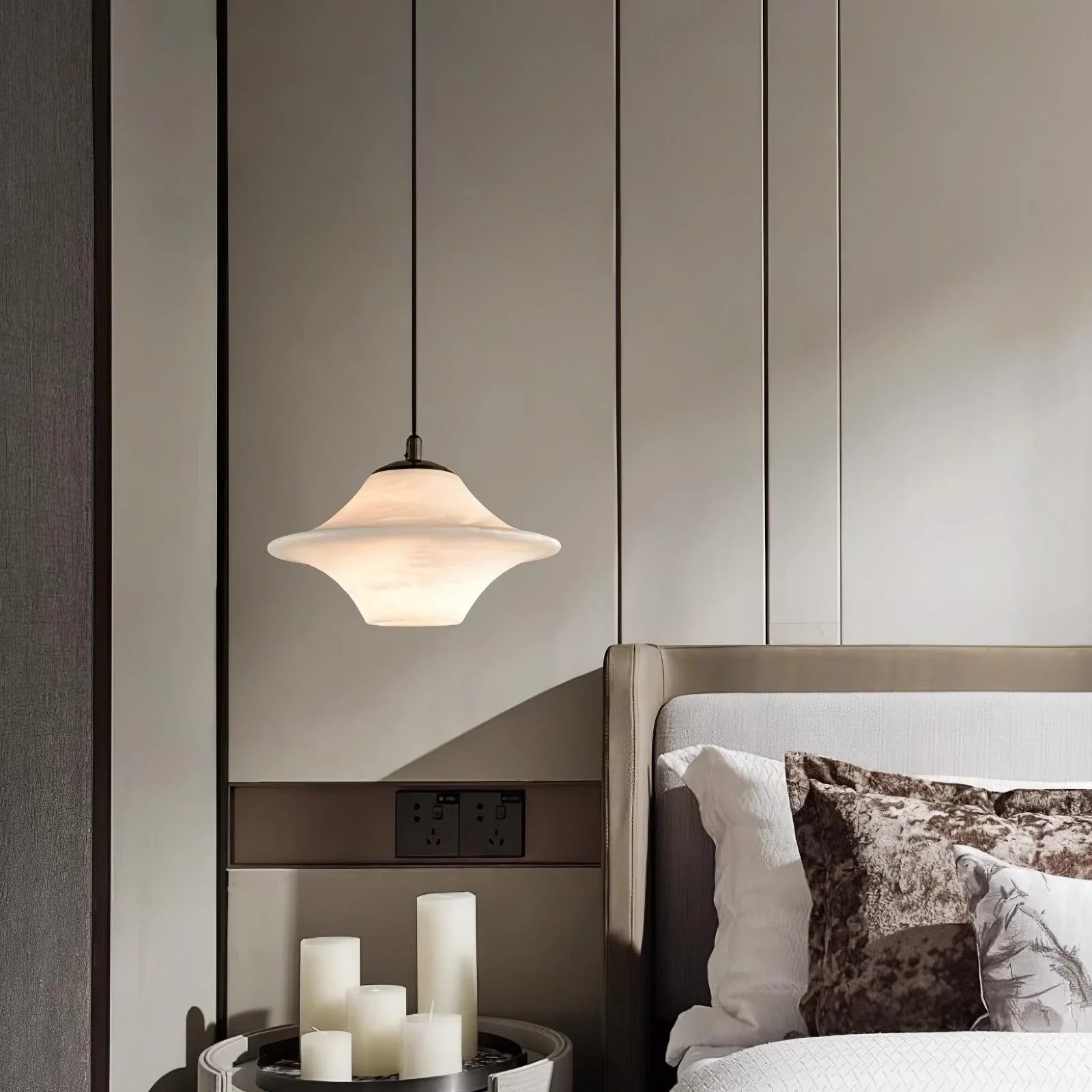 Modern saucer-shaped alabaster pendant lamp hanging above bedside table with white candles in elegant bedroom