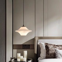 Modern saucer-shaped alabaster pendant lamp hanging above bedside table with white candles in elegant bedroom