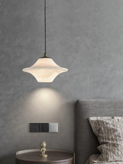 Modern alabaster pendant lamp with black fixture above bedside table and gray upholstered bed