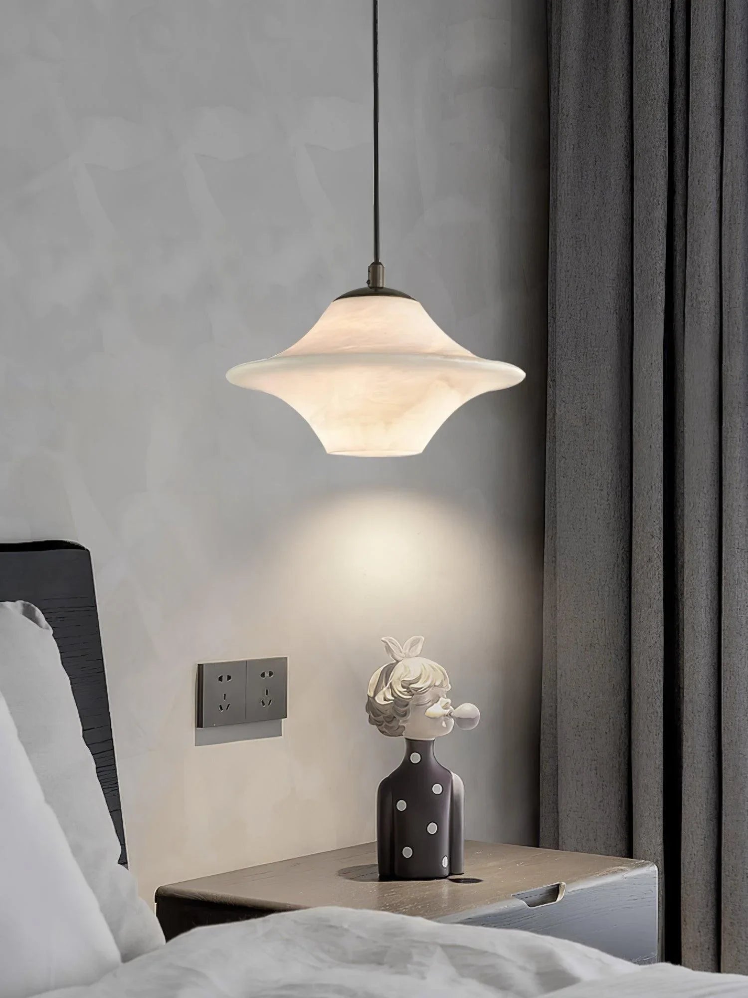 Modern black and white saucer-shaped alabaster pendant lamp hanging over bedside table with decorative bust