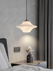 Modern black and white saucer-shaped alabaster pendant lamp hanging over bedside table with decorative bust
