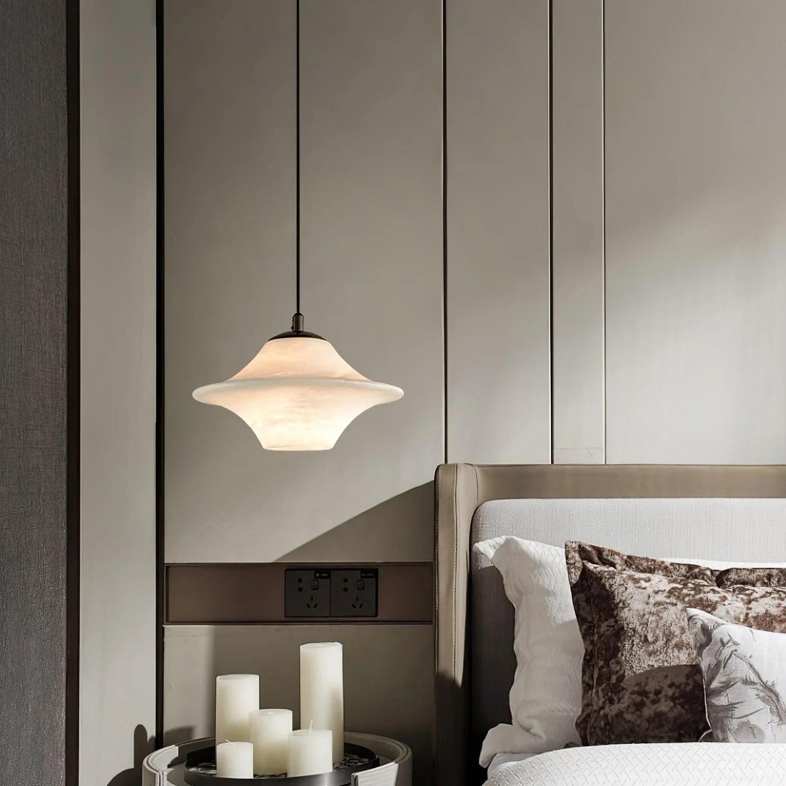 Modern alabaster pendant lamp with black cord above bedside table and bed with decorative pillows