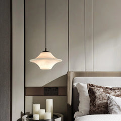 Modern alabaster pendant lamp with black cord above bedside table and bed with decorative pillows