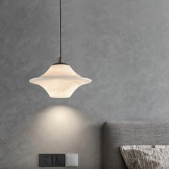 Modern black and white saucer alabaster pendant lamp hanging over a gray textured wall and bed headboard