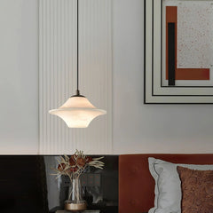 Modern alabaster pendant lamp with black accent hanging above a bedside table with dried flowers in a vase