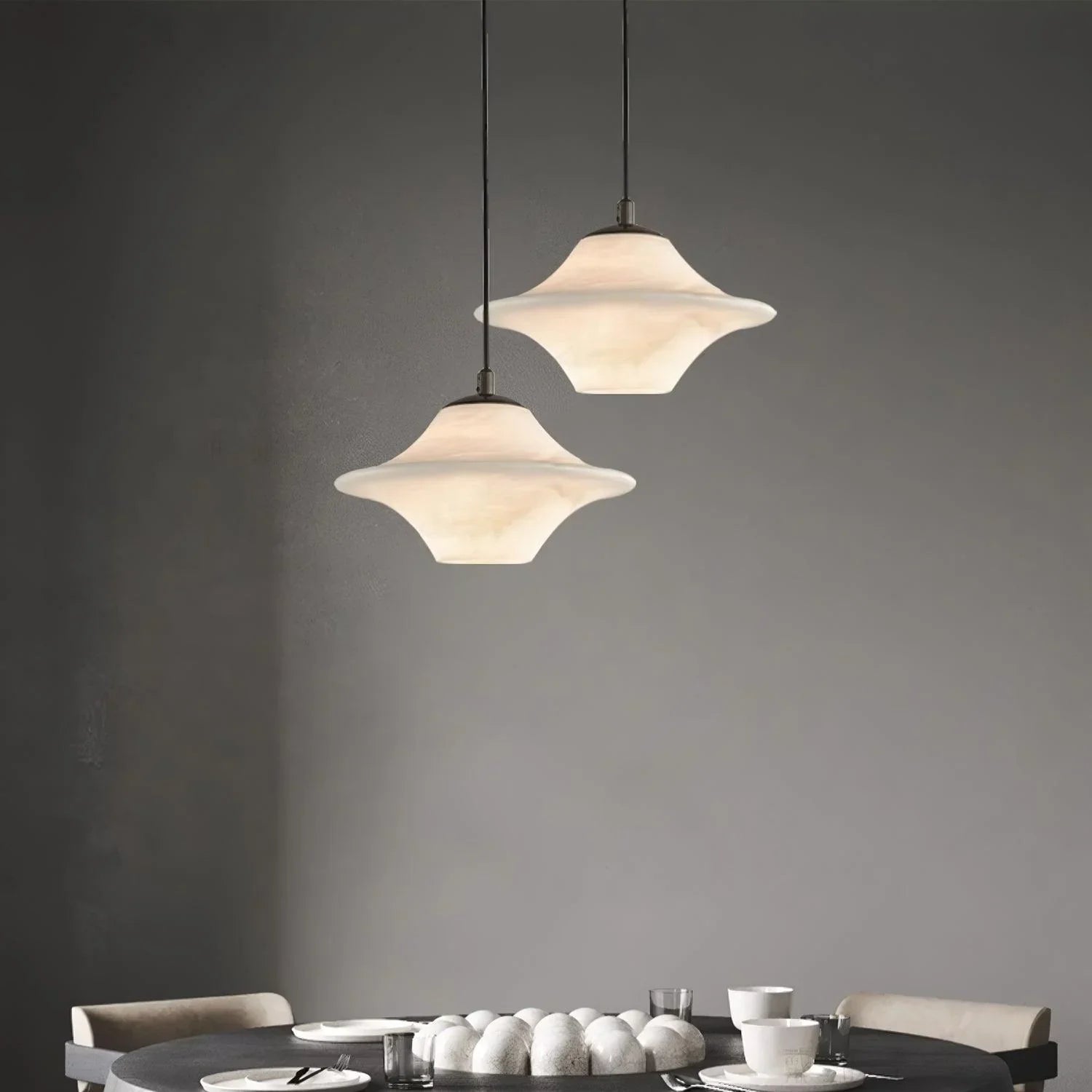 Modern black and white saucer alabaster pendant lamps hanging over a dark round dining table with minimalist tableware