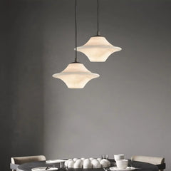 Modern black and white saucer alabaster pendant lamps hanging over a dark round dining table with minimalist tableware