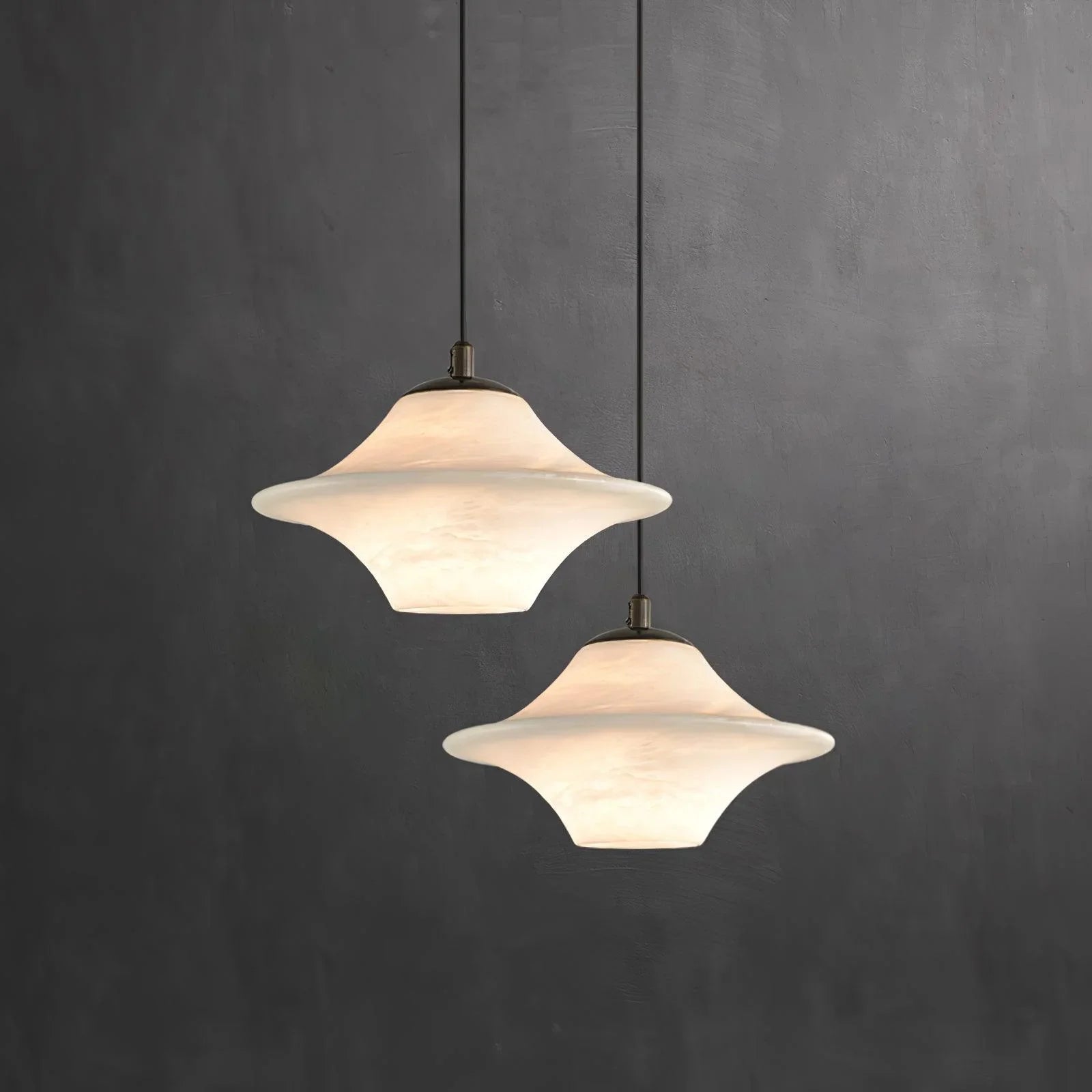 Two alabaster pendant lamps with black ceiling mounts against textured dark gray wall