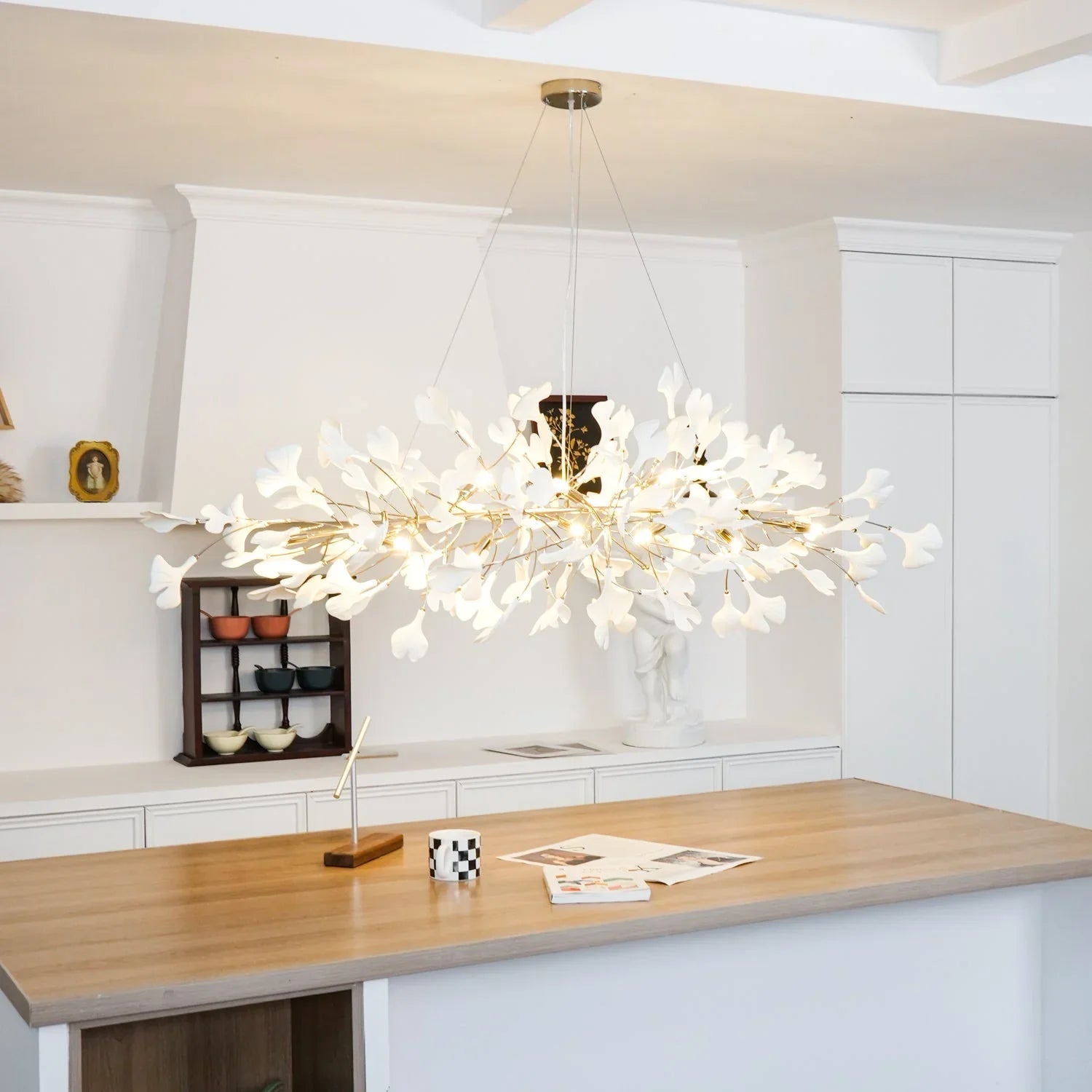 Modern gold and white Gingko leaf chandelier pendant lamp over wooden kitchen island in bright minimalist room