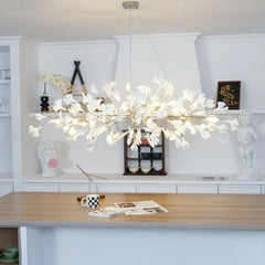 Modern gold and white ginkgo leaf chandelier pendant lamp hanging over wooden dining table in stylish room with decorative sculptures