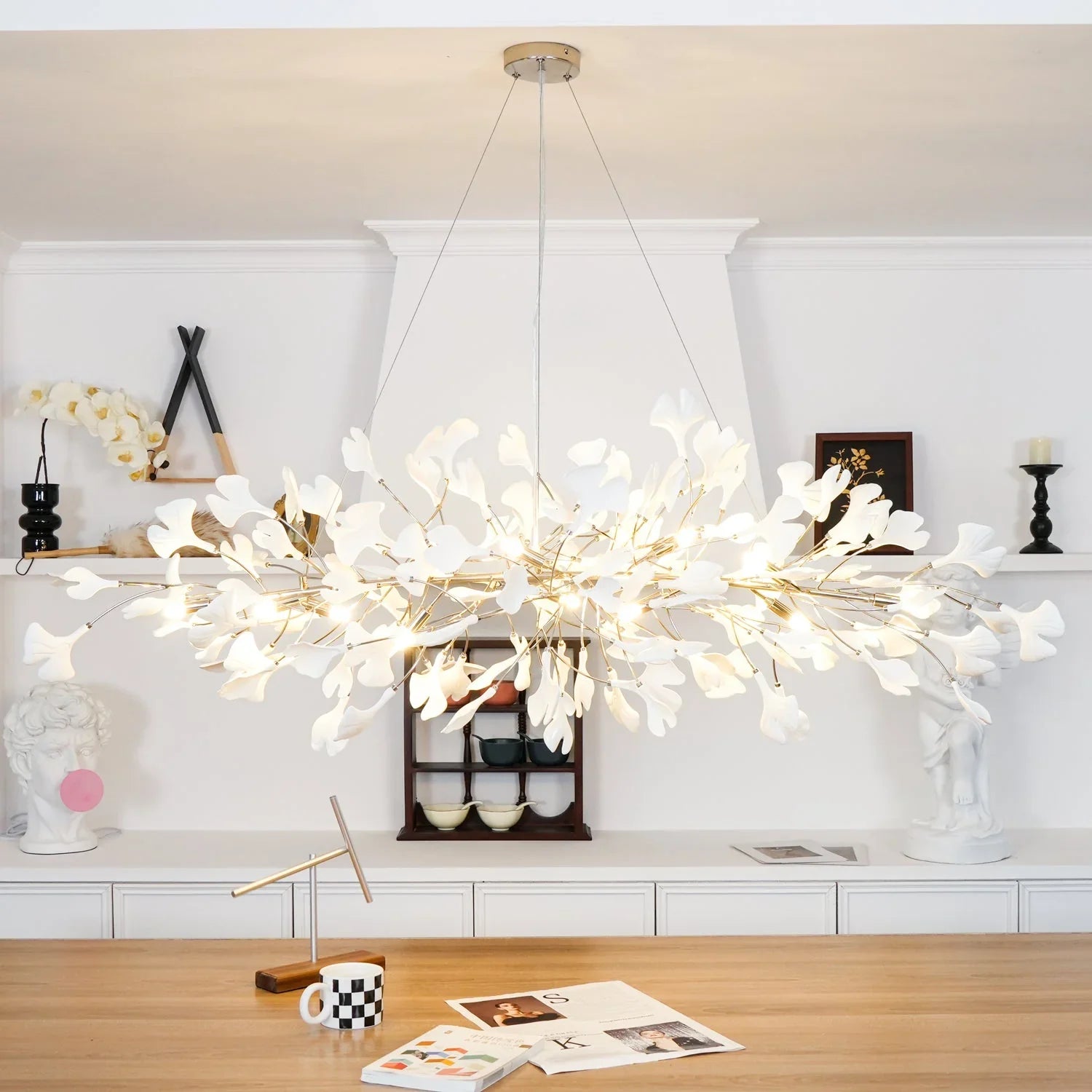 Modern gold and white gingko leaf chandelier pendant lamp hanging above wooden table in stylish interior