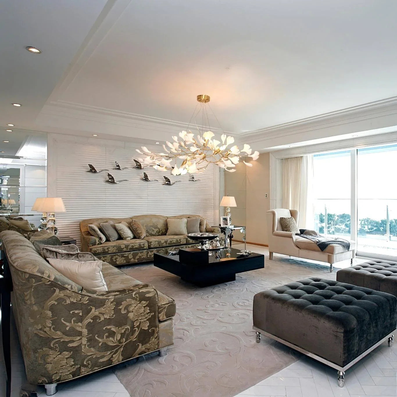 Modern elegant living room with floral patterned sofas, chaise lounge, black coffee table, tufted ottomans, and gold white gingko chandelier
