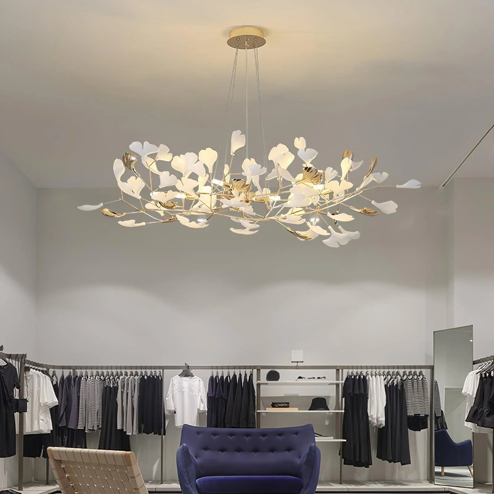 Modern gold and white gingko leaf chandelier pendant lamp in minimalist boutique with clothing racks and navy sofa
